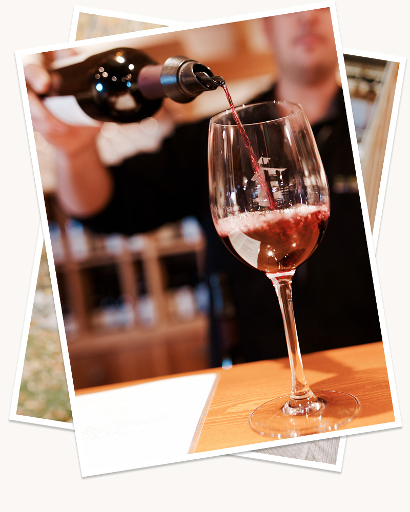 A Hillside Winery employee blurred in the background, pouring a glass of wine on a wooden table in the foreground. 