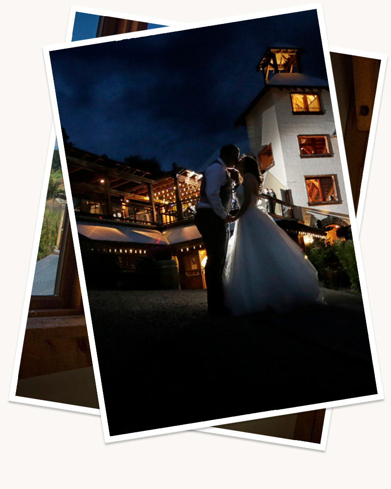 Two digitally stacked images, the top, visible image, showing a newly married couple, in their wedding dress and tux, kissing in front of the Hillside Winery venue, the warm lights gently lighting up the husband and wife, with dark blue skies above them. 