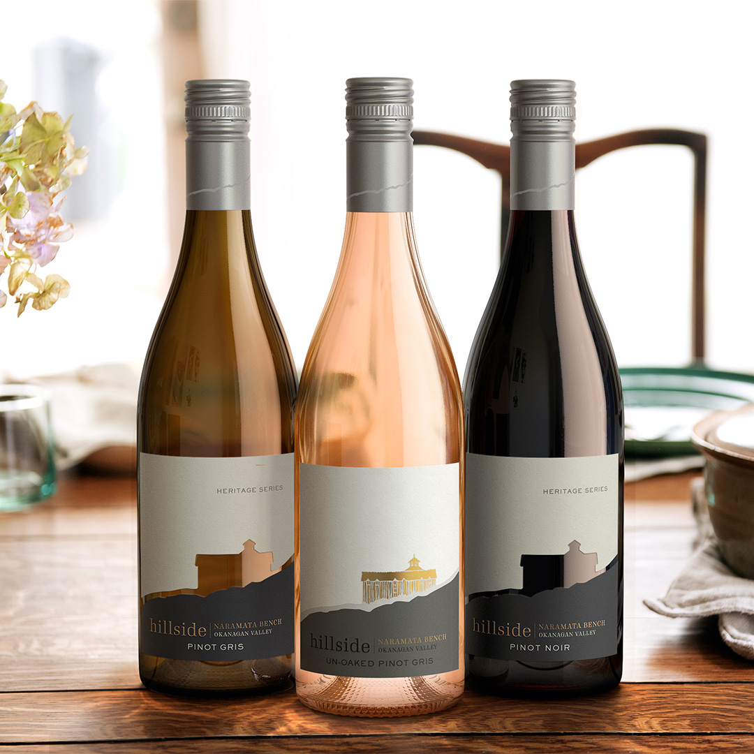 Three Hillside Winery wine bottles placed in a triangle on a dark, wood table. The left most bottle being the winery's Pinot Gris, the centred bottle being an Un-Oaked Pinot Gris, and lastly, the right bottle being a Pinot Noir. 