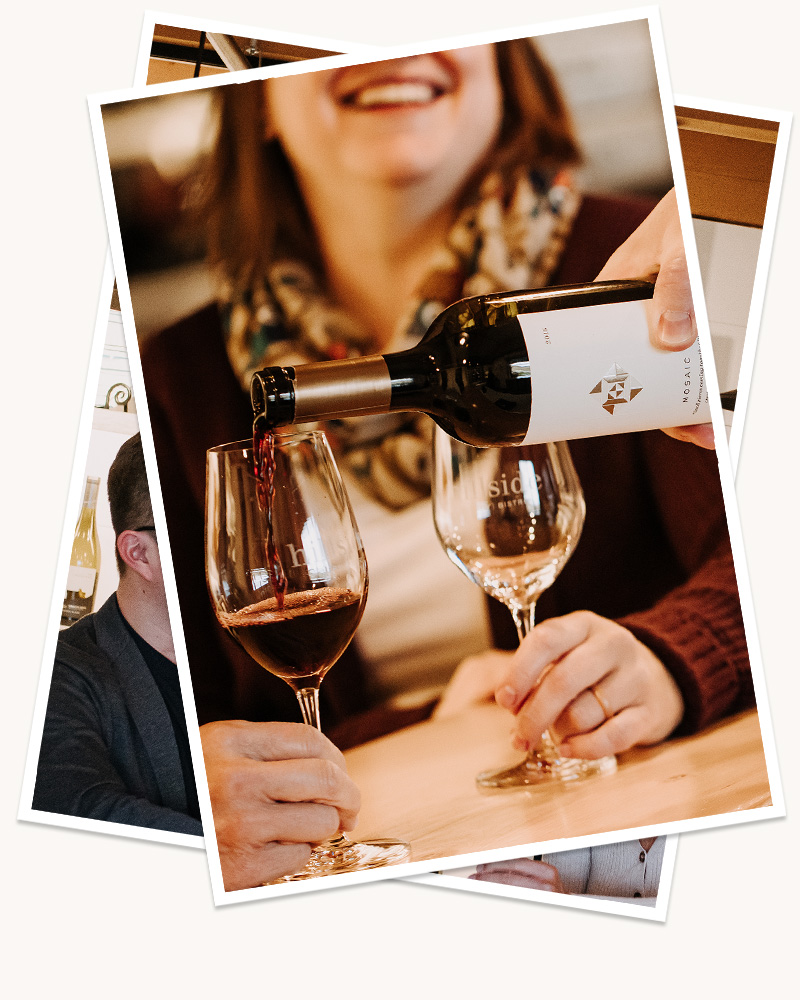 A blurred woman in the background, smiling as two glasses in the foreground are filled with Hillside Winery wine. 