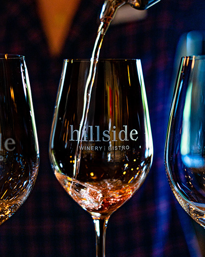 3 glasses of wine with the Hillside Winery logo on them, with one wine glass being poured into