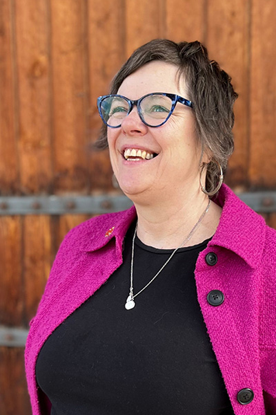 A grinning image of Wine Shop Manager, Lesley Buxton, gazing off to the left of the camera. 